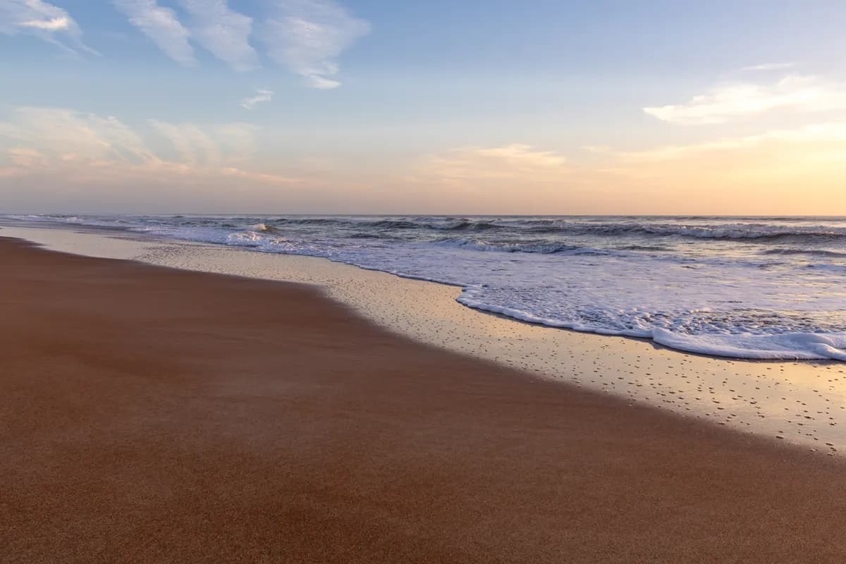 Sandy beach shoreline with gentle waves during a calm sunset.