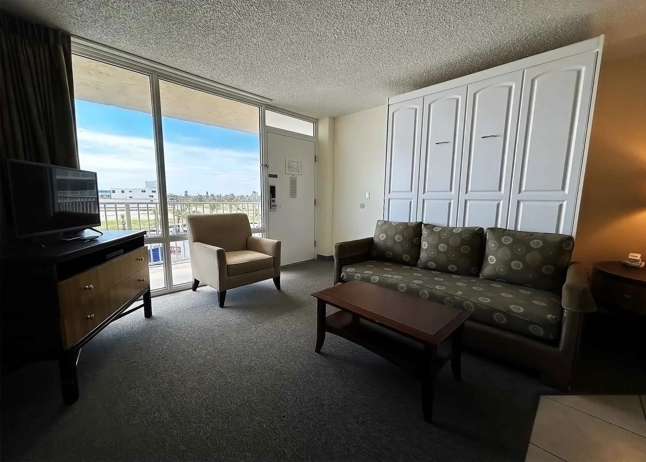 Studio living area with sofa bed, armchair, coffee table, and sliding door to balcony.
