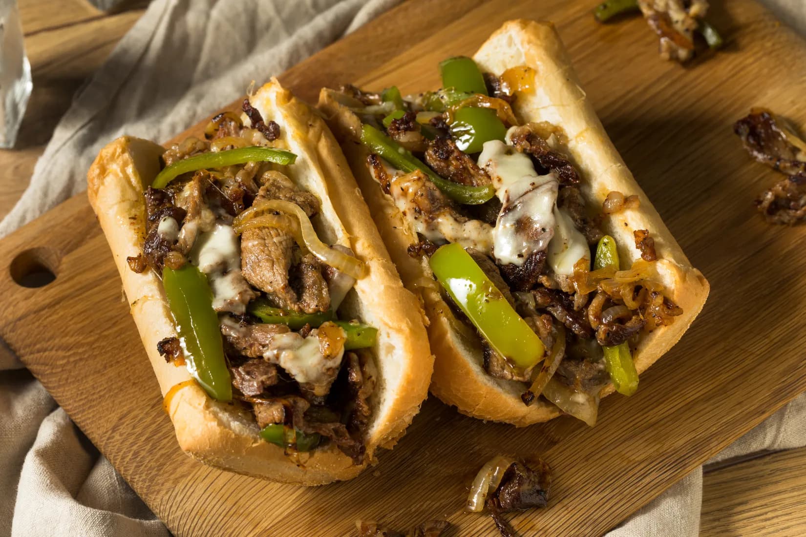 Close-up of a cheesesteak sandwich filled with sliced beef, sautéed onions, green peppers, and melted cheese on a toasted roll.